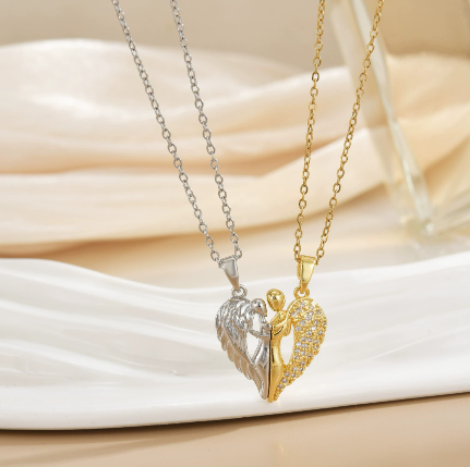 Colliers duo en acier inoxydable, pendentif cœur divisé en deux moitiés : une moitié argentée avec ailes d’ange sculptées et une moitié dorée ornée de pierres scintillantes, présentés sur une assiette blanche