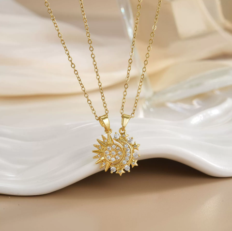 Duo de colliers Célunéa Cristal dorés, pendentifs soleil et lune sertis de pierres blanches scintillantes, présentés sur assiette blanche
