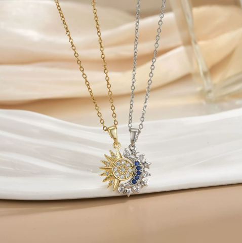 Duo de colliers Célunéa dorés, pendentifs soleil et lune sertis de pierres blanches et bleues, présentés sur assiette blanche.