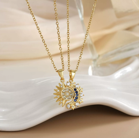 Duo de colliers Célunéa dorés, pendentifs soleil et lune sertis de pierres blanches et bleues, présentés sur assiette blanche.