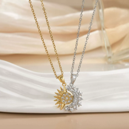 Duo de colliers Célunéa Cristal bicolores, un collier doré et un collier argenté, pendentifs soleil et lune sertis de pierres blanches, présentés sur assiette blanche