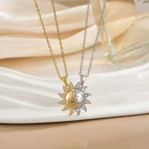 Duo de colliers soleil bicolores, un doré et un argenté, pendentifs sertis de pierres, présentés sur assiette blanche.