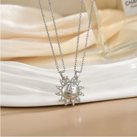 Duo de colliers soleil argentés en acier inoxydable, pendentifs sertis de pierres, présentés sur assiette blanche.